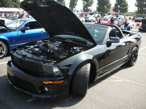 2004 Ford Crown Victoria - Black convertible Mustang at a car show, hood open to display the engine bay.