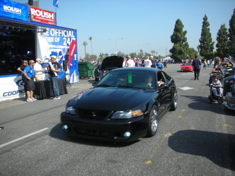2004 Ford Crown Victoria - A black Ford Mustang is driven past a display booth at a car show.