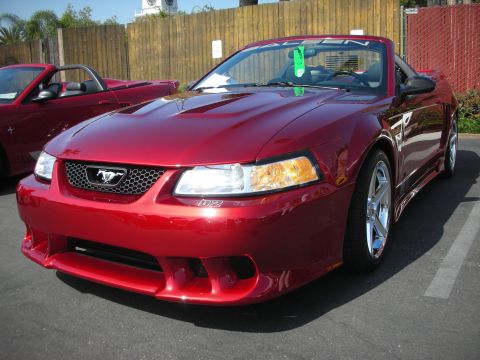 2004 Ford Crown Victoria - Two red convertible Mustangs are parked in a lot. The front car is a 2000 model.