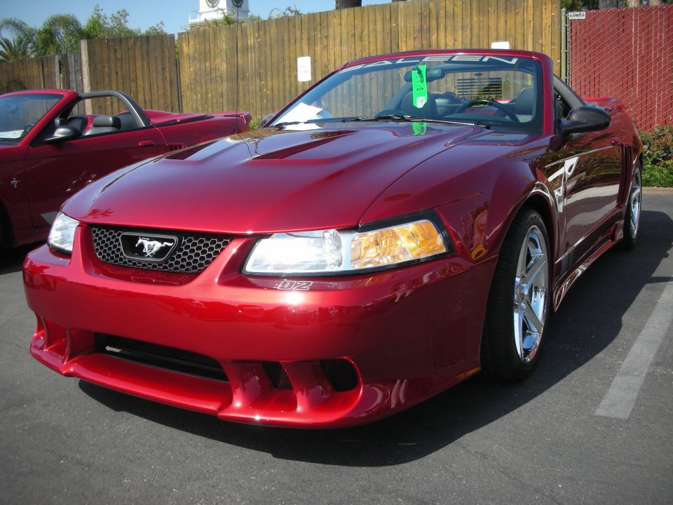 Red convertible Mustang with a black soft top, parked next to another red convertible