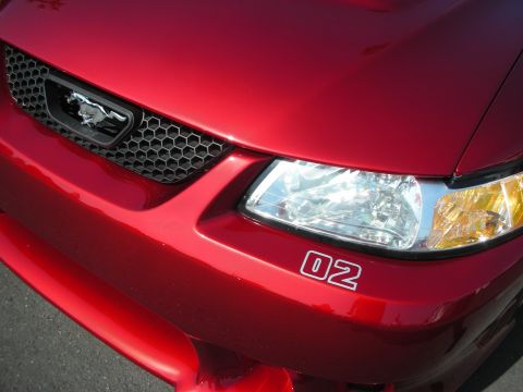2004 Ford Crown Victoria - Close-up of a red Ford Mustang's front grille and headlight, a prominent '02' decal.