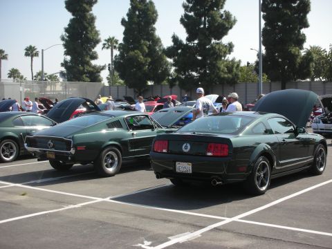 2004 Ford Crown Victoria - Two dark green Ford Mustangs are parked at an outdoor car show, one from the mid-2000s and another from an earlier generation.