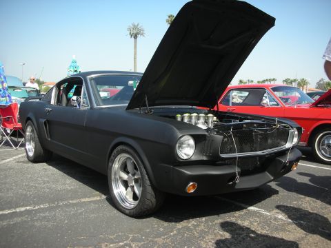 2004 Ford Crown Victoria - A matte black 1965 Ford Mustang is displayed with its hood open, revealing a custom engine setup at a car show.