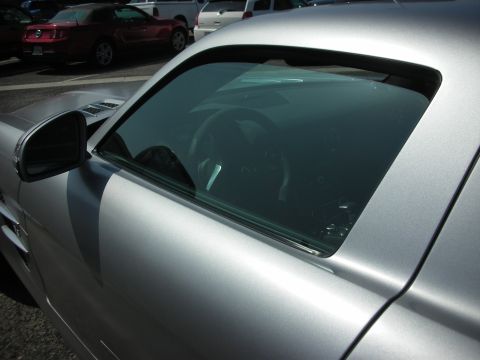 2004 Ford Crown Victoria - Close-up of a silver sports car's interior, showing the steering wheel and dashboard through the tinted side window. Other vehicles are vis…