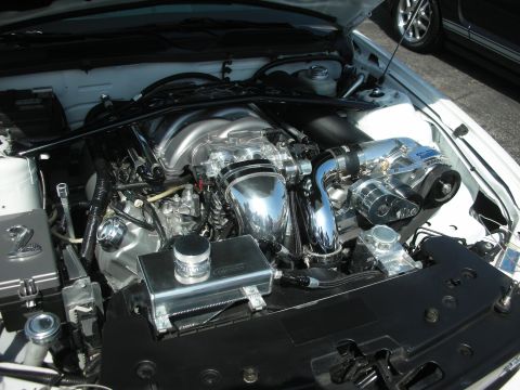 2004 Ford Crown Victoria - The engine bay features a polished supercharger and intake manifold, with another vehicle visible in the background.
