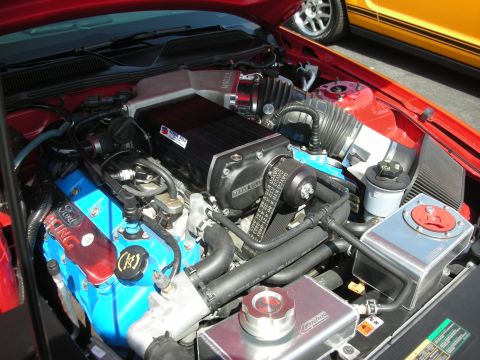 2004 Ford Crown Victoria - The engine bay features a prominent black supercharger and blue Ford Racing valve covers, with another vehicle visible in the background.