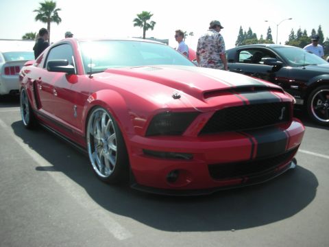2004 Ford Crown Victoria - A red Ford Mustang Shelby GT500 is parked at an outdoor event, with other vehicles and people in the background.