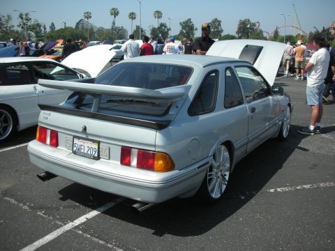 2004 Ford Crown Victoria - A silver hatchback with a prominent rear spoiler and aftermarket wheels is displayed at an outdoor car show, with other vehicles and specta…
