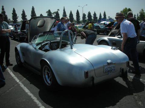 2004 Ford Crown Victoria - A silver Shelby Cobra replica is displayed at a car show with other vehicles and spectators.