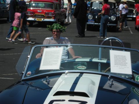 2004 Ford Crown Victoria - A man wearing a green wig sits in a convertible at a car show with other vehicles in the background.