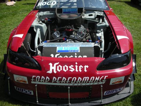 2004 Ford Crown Victoria - Front view of a red racing car with its hood open, revealing the engine and various sponsor decals.