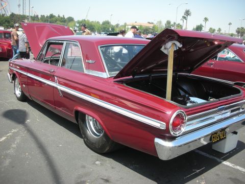 2004 Ford Crown Victoria - A red 1963 Ford Falcon sedan is displayed with its hood and trunk open at an outdoor car show.