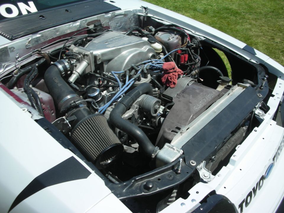 Engine bay of a white car with a Ford V8 engine, aftermarket air intake, and radiator