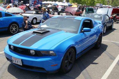 1992 Ford Taurus - Blue 2010 Ford Mustang GT with black racing stripes at a car show.