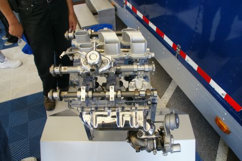 1992 Ford Taurus - Engine with turbocharger on display stand next to a blue truck.