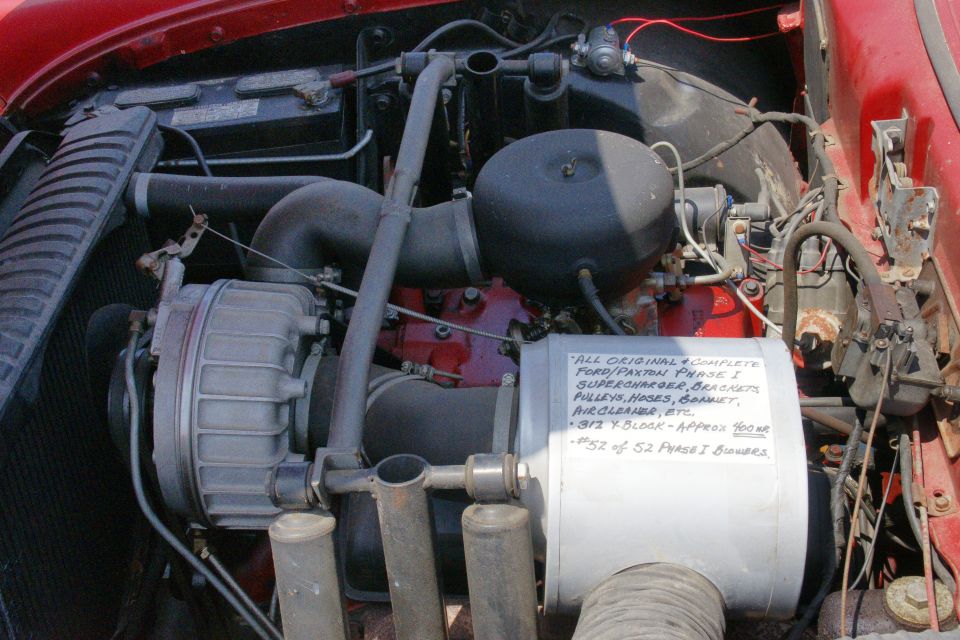 Engine bay with a supercharger, air cleaner, and a handwritten note. Red car exterior visible