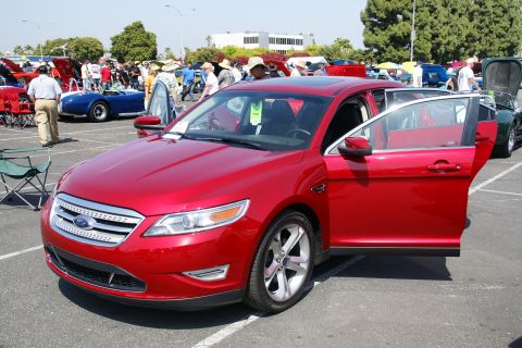 1992 Ford Taurus - A red Ford sedan is displayed with its doors open at an outdoor car show.