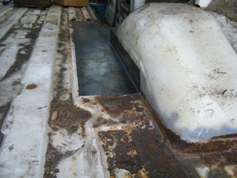 1981 Ford E350 - The interior floor of a van shows significant rust damage, with a section of new metal recently installed.