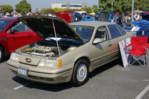 1992 Ford Taurus - A gold 1992 Ford Taurus sedan is displayed with its hood open at an outdoor car show.