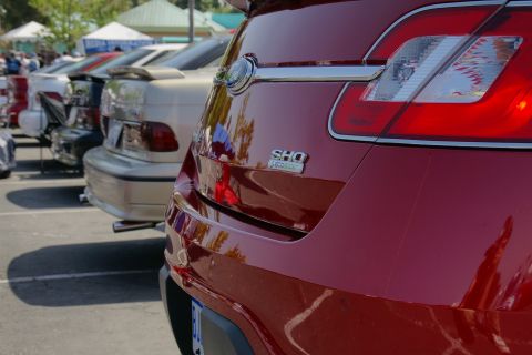1992 Ford Taurus - The rear of a red SHO Taurus, a chrome strip and distinctive taillight design, parked in a lot with other vehicles.