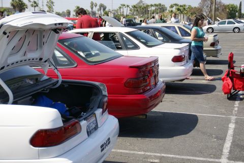 1992 Ford Taurus - Several cars are parked in a lot, with the trunks of two cars open. A woman walks by in the background.