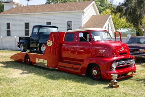 1992 Ford Taurus - A vintage red tow truck, likely from the 1950s, is shown carrying a black pickup truck on its trailer, with a trophy displayed nearby.