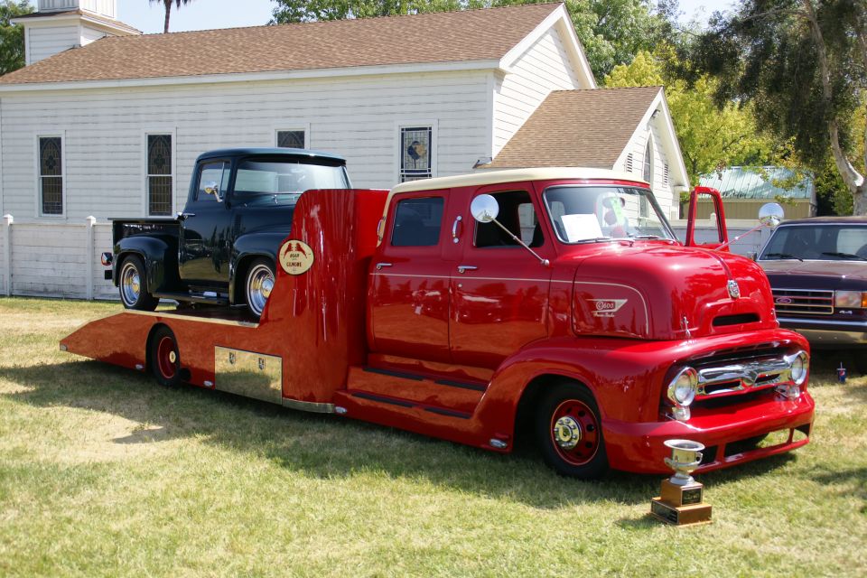 Red tow truck with cream roof carrying a black pickup truck. Trophy in foreground