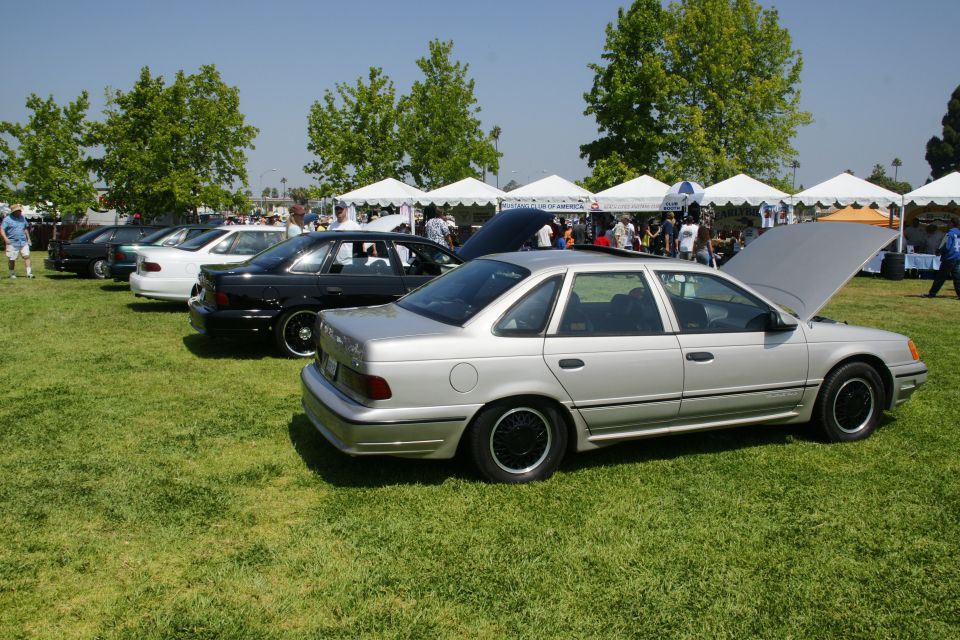 Silver 1992 Ford Taurus with hood up, parked on grass at an outdoor event with other cars and tents