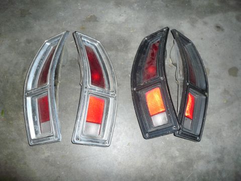 1975 Ford Ranchero - Two pairs of tail lights, one set with chrome trim and the other with black housings, are displayed on a concrete surface.