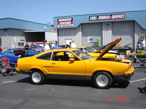 1978 Ford Mustang II - A yellow 1978 Ford Mustang II coupe is displayed with its hood open, alongside other vehicles.