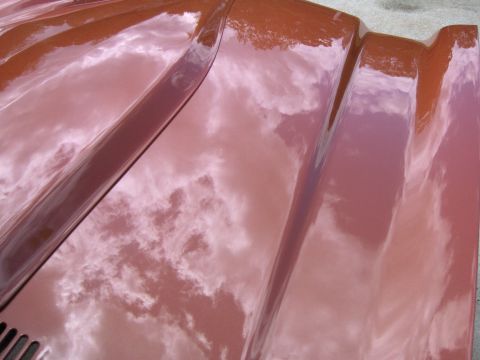 1980 Chevrolet Camaro - Reflections of clouds are visible on the glossy surface of a red car hood.