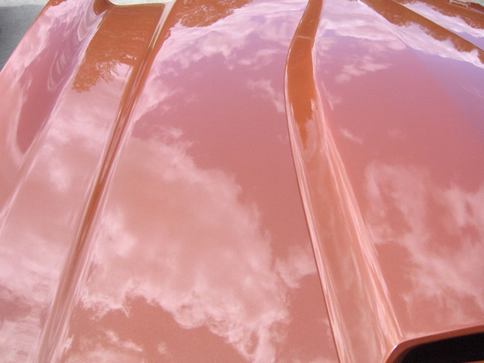Close-up of a shiny orange car hood with reflections of clouds