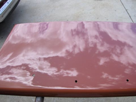 1980 Chevrolet Camaro - The reflection of clouds on a red car hood is visible, with three small holes drilled into the surface.