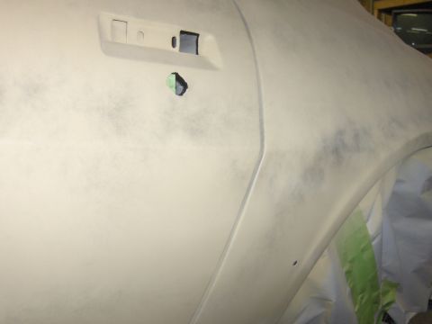1980 Chevrolet Camaro - A close-up view of a 1980 Chevrolet Camaro's side, prepared for painting with primer and masking.