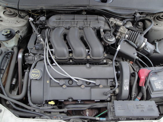 Engine bay of a transverse V6 with black intake manifold and red battery terminal