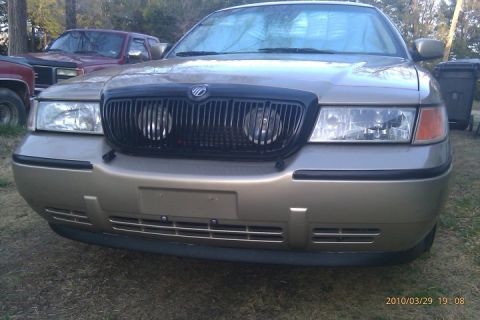 2000 Mercury Grand Marquis - Front view of a 2000 Mercury Grand Marquis with a black grille. Another vehicle is parked nearby.