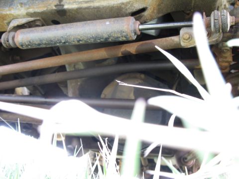1978 Ford Bronco - This image shows the underside of a vehicle, focusing on the steering and suspension system, with grass obscuring parts of the view.