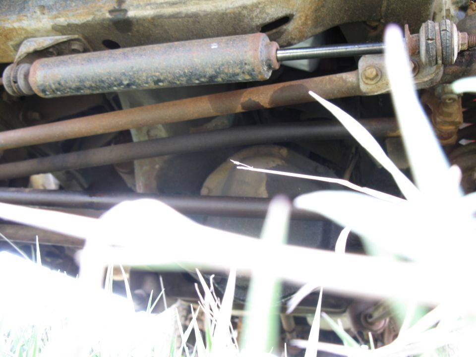 Undercarriage view of a vehicle, showing steering components and suspension parts. Some grass is in the foreground