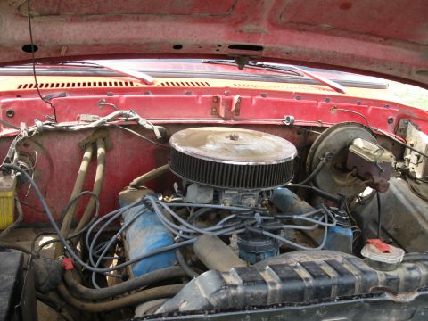 1978 Ford Bronco - The engine bay of a red 1978 Ford Bronco shows its V8 engine, carburetor, and air filter, with the radiator and brake fluid reservoir also…