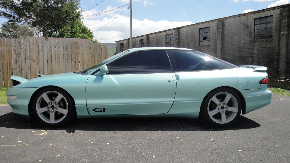 Light teal-green sports coupe in profile with GT badge and alloy wheels