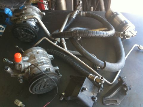 1987 Suzuki Samurai - Various automotive parts, including AC compressors and hoses, are laid out on a workbench.
