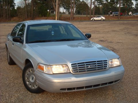 2003 Ford Crown Victoria - A silver Ford Crown Victoria is parked on a gravel lot with trees in the background.