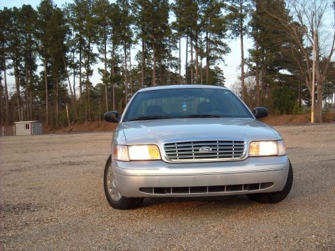 2003 Ford Crown Victoria - Front view of a silver 2003 Ford Crown Victoria parked on a gravel lot with trees in the background.