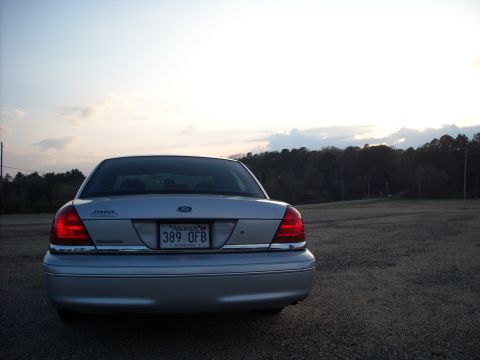 2003 Ford Crown Victoria - The rear of a silver Ford Crown Victoria is shown parked in an open area during the day.
