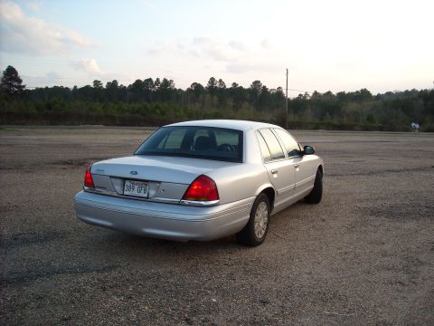2003 Ford Crown Victoria - A silver 2003 Ford Crown Victoria is seen from the rear on a gravel lot with trees in the background.