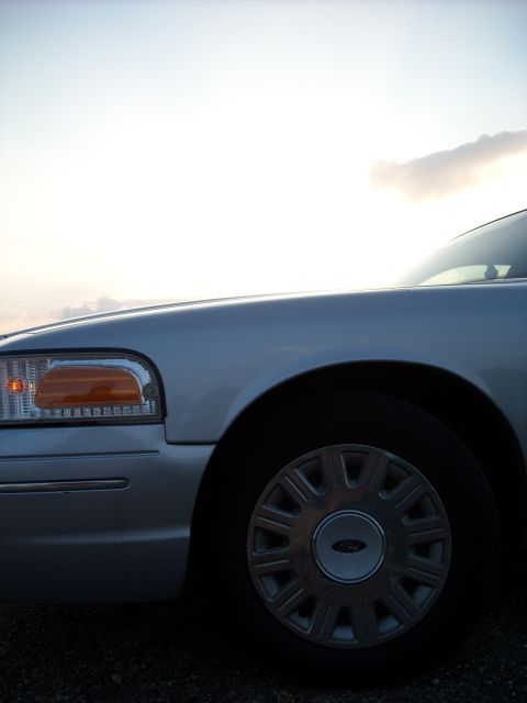2003 Ford Crown Victoria - The front quarter panel and wheel of a silver Ford Crown Victoria are visible under a bright sky.