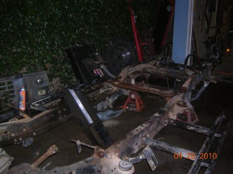 1985 Ford Bronco - The chassis of a vehicle is disassembled and supported by jack stands in an outdoor setting.