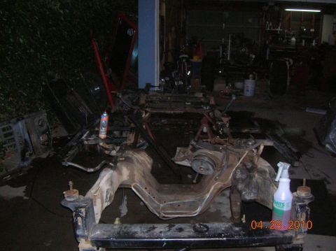 1985 Ford Bronco - Disassembled vehicle chassis and frame in a workshop setting, with tools and parts scattered around.