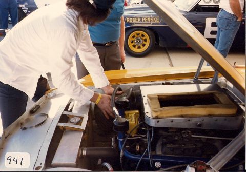 1973 Ford Mustang - Mechanic attends to the engine of a race car, with another Penske-sponsored vehicle visible behind.