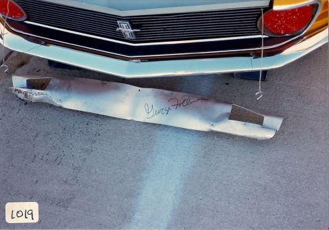 1973 Ford Mustang - A bent exhaust pipe with a signature is shown beneath the front grille of a car.